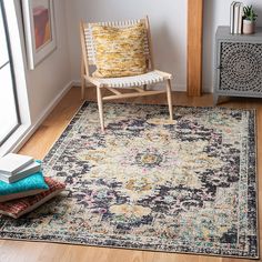 a room with a chair, rug and books on the floor in front of a window