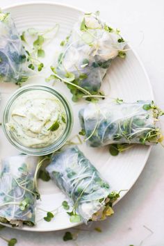 spring rolls on a plate with dip in the middle and green sprouts around them