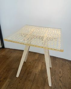 a glass table with wooden legs and dots on the top, in front of a white wall