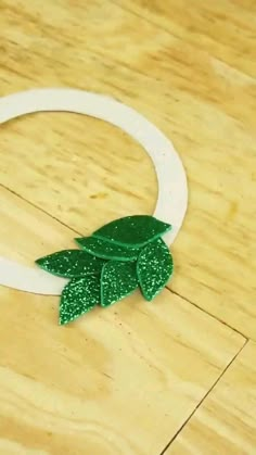 a close up of a paper wreath on a wooden floor with green leaves and glitters