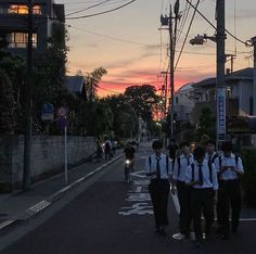 a group of young men walking down a street at sunset with backpacks on their backs