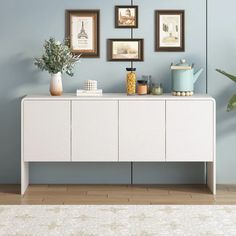 a white dresser with pictures on the wall and plants in vases next to it