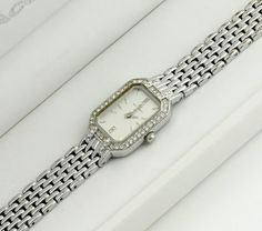 This silver-colored watch boasts a rectangular case surrounded by stones, adding a touch of elegance and sparkle. The grey metallic dial is also adorned with stones, enhancing its luxurious appeal. Paired with a classic metal bracelet, the watch strikes a balance between simplicity and brilliance. It's a sleek, bright, and elegant accessory that stands out for its understated glamour and sophistication. Dimensions: Bracelet Length: up to 16 cm (6.3 inches) - adjustable Case Width: 1.7 cm (0.4 inches) Case Height: 2.3 cm (0.9 inches) Bracelet Width: 1 cm (0.4 inches) Condition: The watch is in good condition, with minor wear on the bracelet and a tiny chip on the glass between the 3 and 4-hour marks, details in the photo. All presented watches are tested and in working condition, also equip Silver Diamond Watch With Diamond Accents As Gift, Rectangular Diamond Watch As A Gift, Silver Rectangular Diamond Watch For Anniversary, Rectangular Diamond Watch As Gift, Rectangular Diamond Watch For Gifting, Elegant Rectangular Diamond Watch For Anniversary, Elegant Rectangular Stainless Steel Watch, Formal Rectangular Diamond Watch With Metal Dial, Elegant Rectangular Diamond Watch With Metal Dial