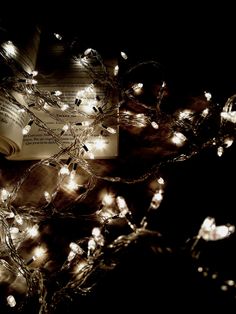 an open book with fairy lights on it sitting next to a pile of books that have been wrapped in string lights