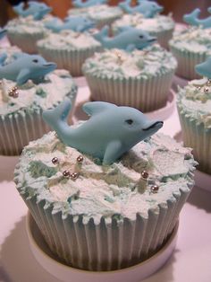 cupcakes decorated with blue and white frosting are sitting on a plate in the shape of dolphins