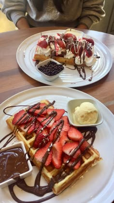 two white plates topped with waffles covered in chocolate sauce and strawberries next to ice cream