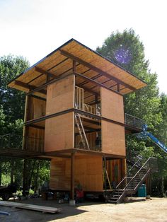 a large wooden structure sitting in the middle of a forest with stairs leading up to it