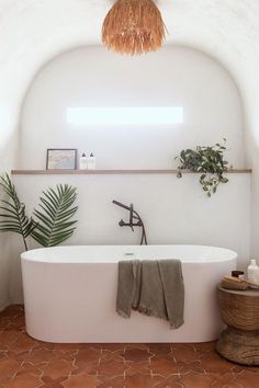 a white bath tub sitting under a window next to a potted plant