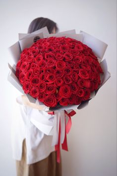 a woman holding a large bouquet of red roses in her hands and wearing a white shirt