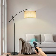 a person holding a remote control in front of a living room with a couch and lamp