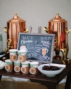 a table topped with coffee cups next to a chalkboard sign that says hot chocolate