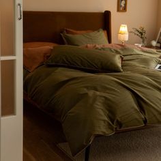 a bed with green sheets and pillows in a bedroom next to a window, near a lamp