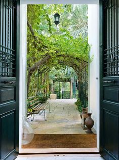 an open door leading to a patio with benches and trees on the other side, surrounded by greenery