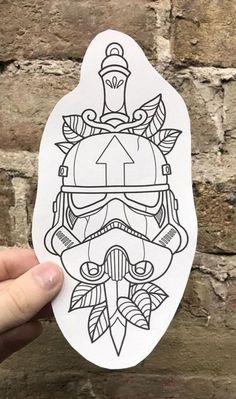 a hand holding up a sticker with a drawing of a trooper helmet on it