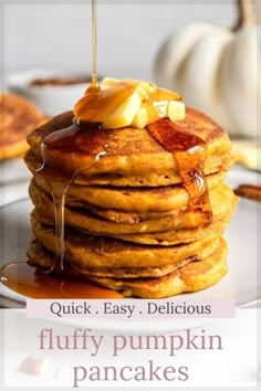 a stack of fluffy pumpkin pancakes with syrup on top and maple syrup being drizzled over them