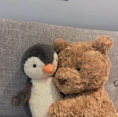 two stuffed animals sitting next to each other on a couch, one is hugging the other