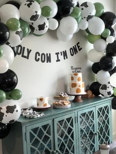 a birthday party with balloons, cake and desserts on a buffet table in front of a cow theme