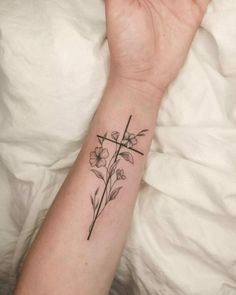 a woman's arm with a cross and flowers tattoo on the left side of her wrist