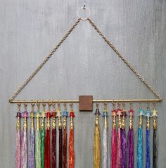 a wall hanging with many different colored tassels and a metal hook on it