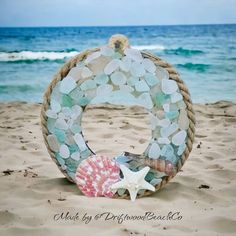 a wreath made out of sea glass and seashells on the beach