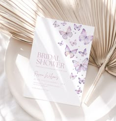 a white plate topped with a purple butterfly bridal shower card next to a fan