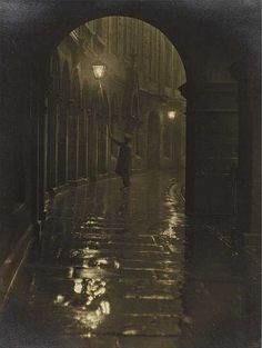 an old black and white photo of a person walking down the street in the rain