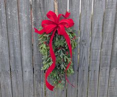 a christmas wreath hanging on the side of a wooden fence with red bows and pine cones