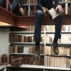 a man sitting on top of a book shelf in front of a bookshelf