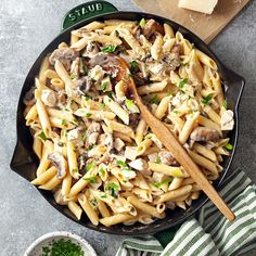 a skillet filled with pasta and mushrooms on top of a table next to some parmesan cheese