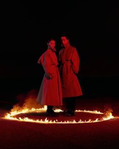 two people standing next to each other in the dark with fire coming from behind them