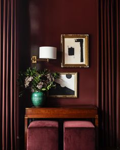 a living room with red walls and two pictures hanging on the wall, one has a green vase filled with flowers