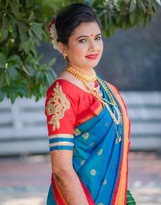 a woman in a blue and red sari standing under a tree with her hands on her hips