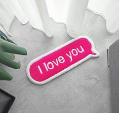 a pink rug with the words i love you on it next to a potted plant