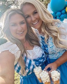 two women dressed in costume posing for a photo with desserts on the table and balloons behind them