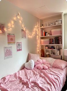 a bed with pink sheets and pillows in a room decorated with lights, bookshelves and pictures on the wall