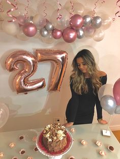 a woman standing in front of a table with a cake and balloons on the wall