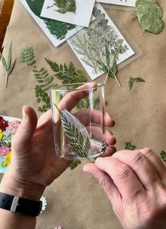 a person holding a glass filled with water surrounded by flowers and leaves on top of a table