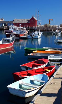 several boats are docked in the water near a dock with a red building behind them