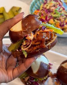 a hand holding a sandwich with meat and vegetables on it, in front of other plates