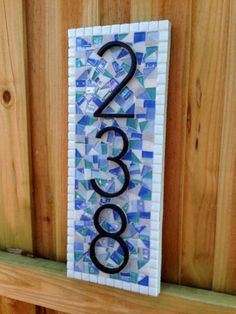 a house number sign on a wooden fence with blue and white mosaic tiles in the shape of numbers