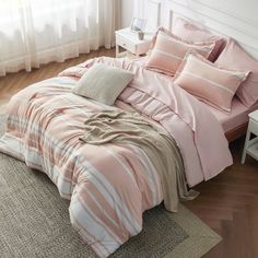 a bed with pink and white striped comforter on top of it next to a window