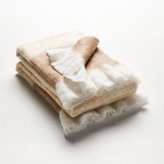 three blankets folded on top of each other with white and brown fringes in them