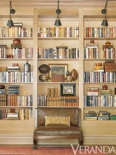 a living room filled with lots of books on top of a wooden book shelf next to a brown leather chair