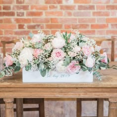 a wooden table topped with a white box filled with lots of pink and white flowers