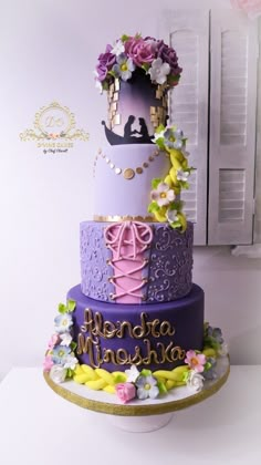 a three tiered cake decorated with purple and pink flowers on a white countertop