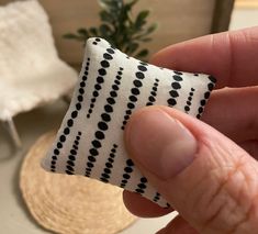 a hand holding a piece of fabric with black dots on it in front of a potted plant