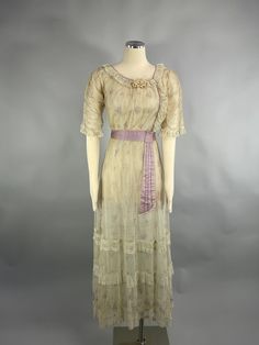 "A rare beautiful authentic 1900's floral print day dress INFO  * Circa - 1900s - 1910 * Label - n/a * Color - beige lavender * Material  - fine netting, silk, satin * Condition - slight fading  to underarms, large older repair to net on skirt   presents beautifully DETAILS - - antique Titanic style dress - inner layer of cream silk - outer layer of printed floral fine net - scoop neckline piped in  lilac - small ribbon rosette at neck - it has a delicate lace ruffle edge - elbow length sleeves with ruched detail - cuffs are edged with ruffle lace - bodice closes with  hooks and eyes - lace and piping hid closure - slight empire waist with satin cummerbund - lilac satin tie falls from waist - hem of skirt has 3 net and ruffle panels - beautiful, delicate, romantic  historical dress PJ10021 Whitepine Aesthetic, 1910 Fashion Women, Floral Net Dress, Tea Attire, 1900 Dresses, 1900 Dress, 1912 Fashion, Edwardian Dresses, Edwardian Gowns