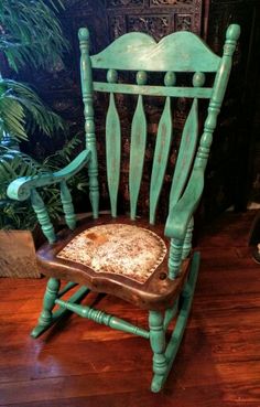 a green rocking chair sitting on top of a wooden floor next to a potted plant