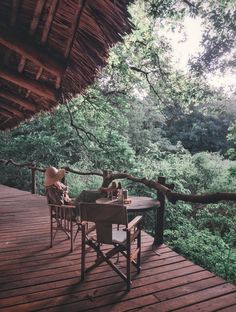 two people sitting at a table on a deck in front of some trees and bushes