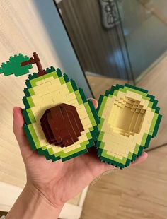 a hand holding two legos made to look like an apple with a tree on top